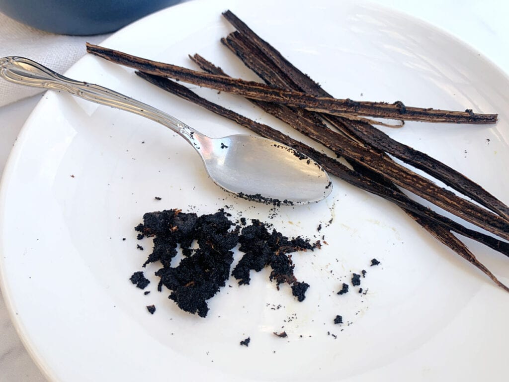 A white plate with a spoon and some vanilla bean pods.