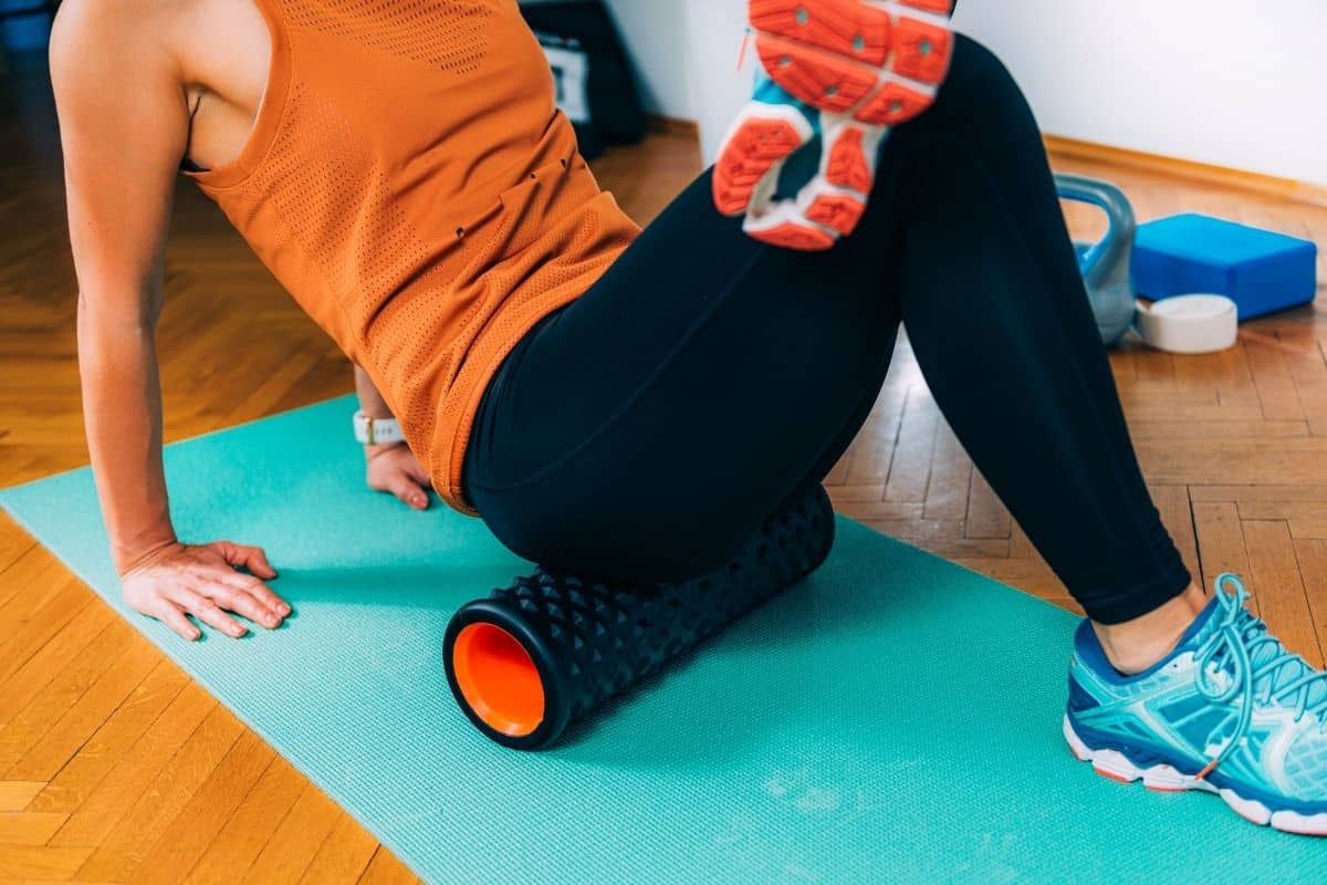 A woman is sitting on a yoga mat with a foam roller.
