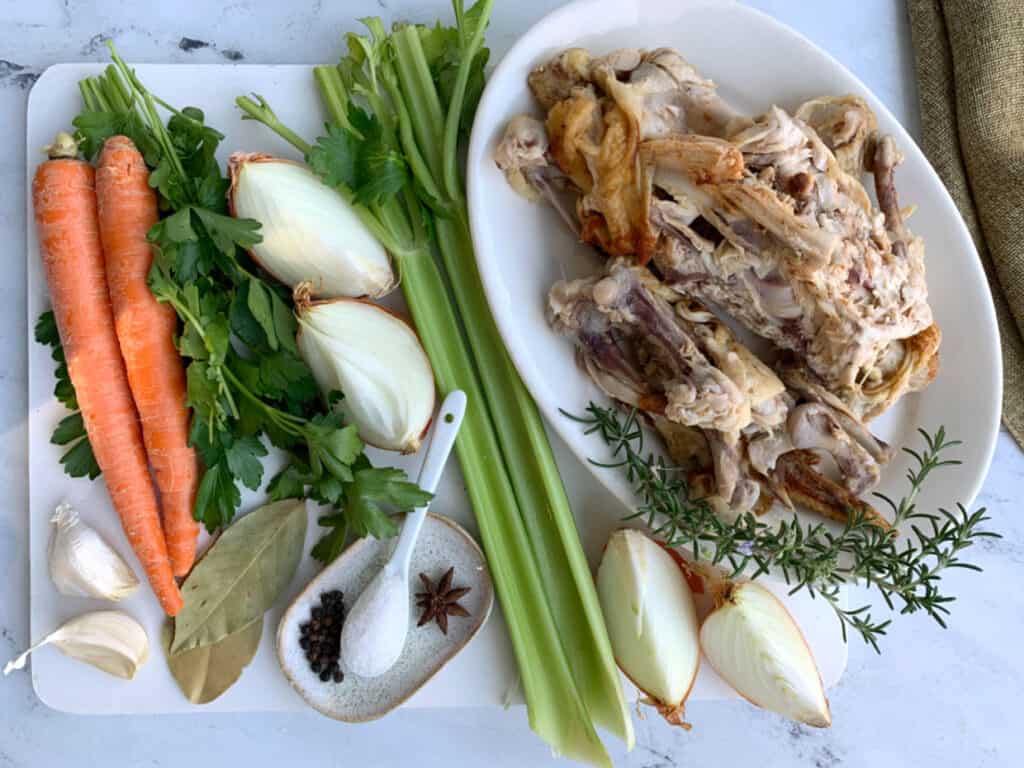A plate with chicken bones, carrots, celery and herbs on it.