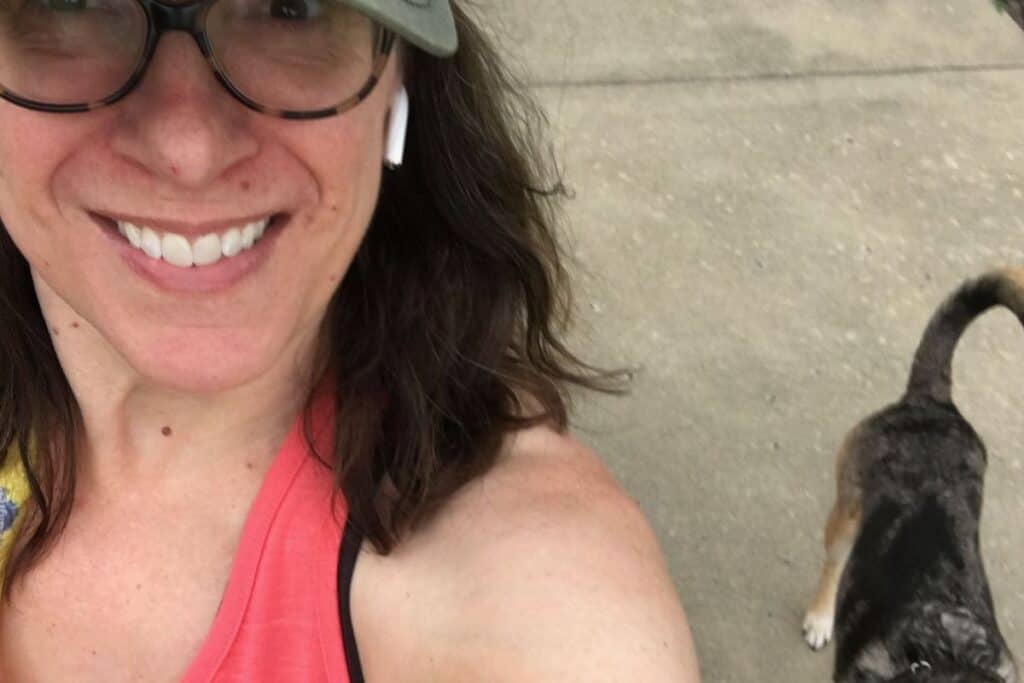 A woman in glasses is taking a selfie with her dog while doing easy at-home workouts.