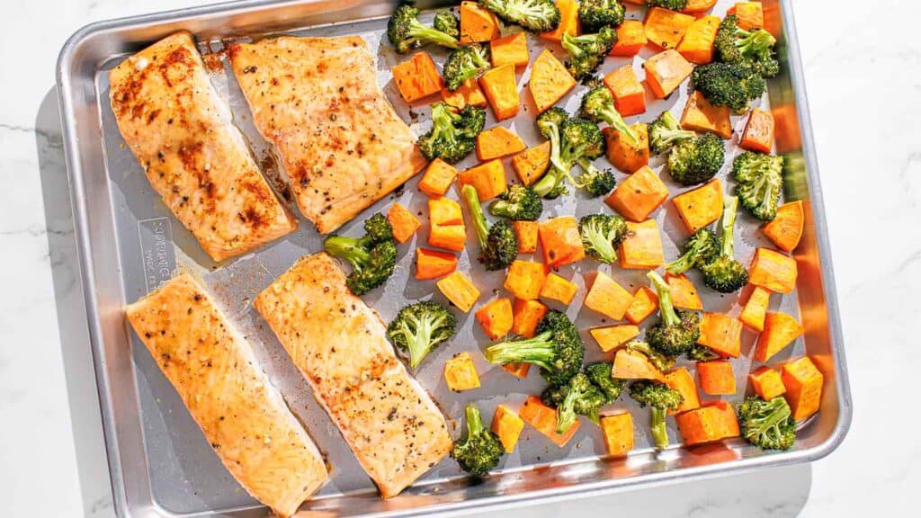 Salmon, broccoli and sweet potatoes on a baking sheet.
