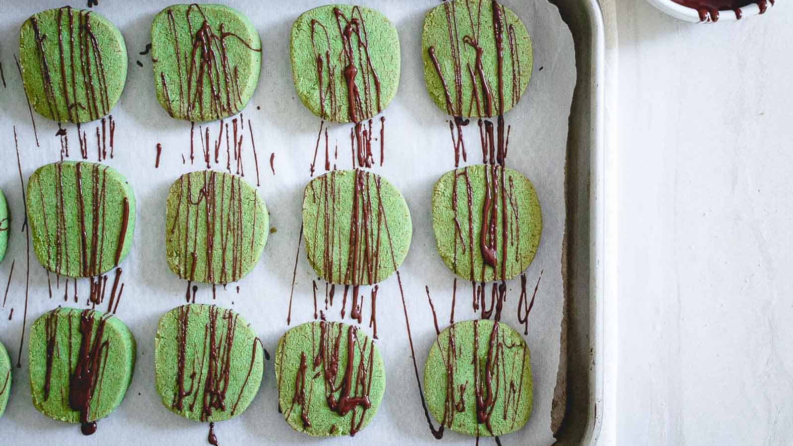 Green cookies with chocolate drizzle on a baking sheet.