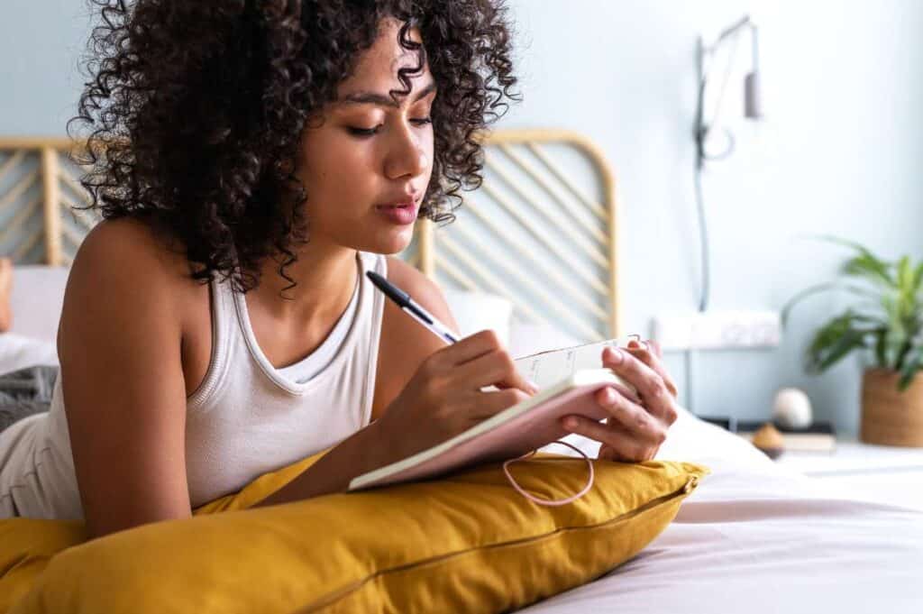 A woman writing in a motivational journal on a bed.