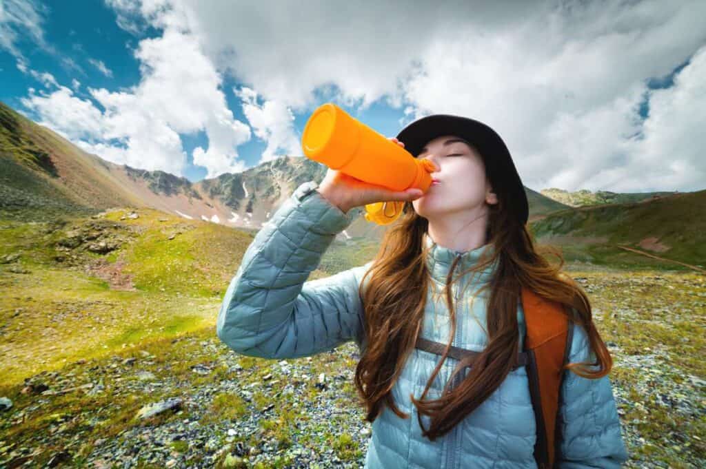 A young woman sipping from a bottle in the mountains, finding motivation through her surroundings.