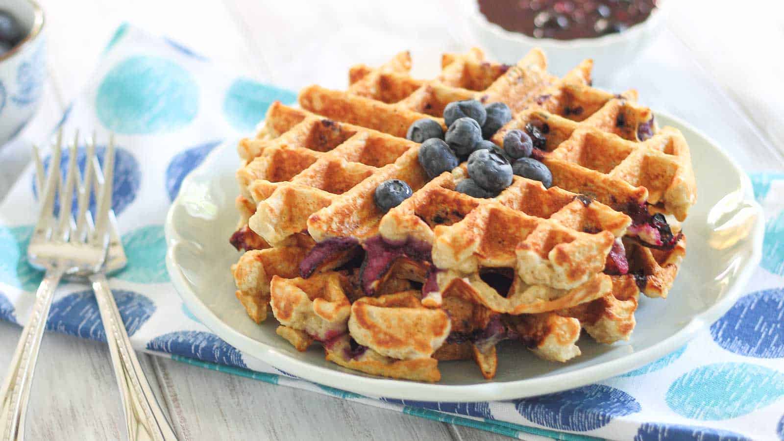 A plate with blueberry waffles with blueberry fruit sauce.