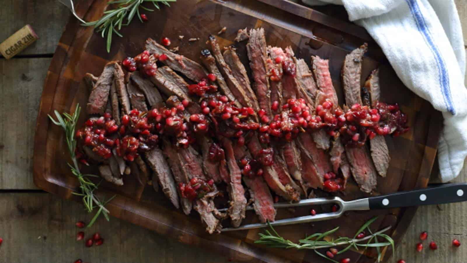 A steak with pomegranate and rosemary on a cutting board.