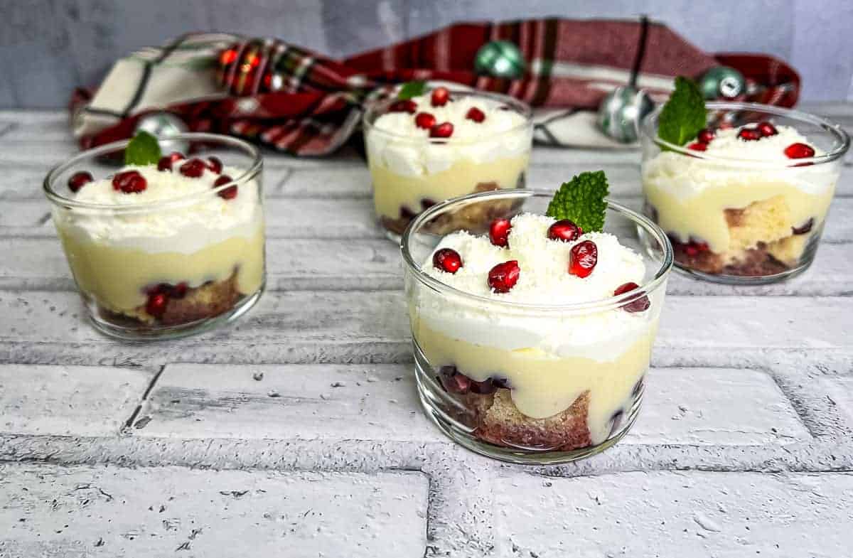 Four glasses of white chocolate pomegranate trifle on a white brick wall.