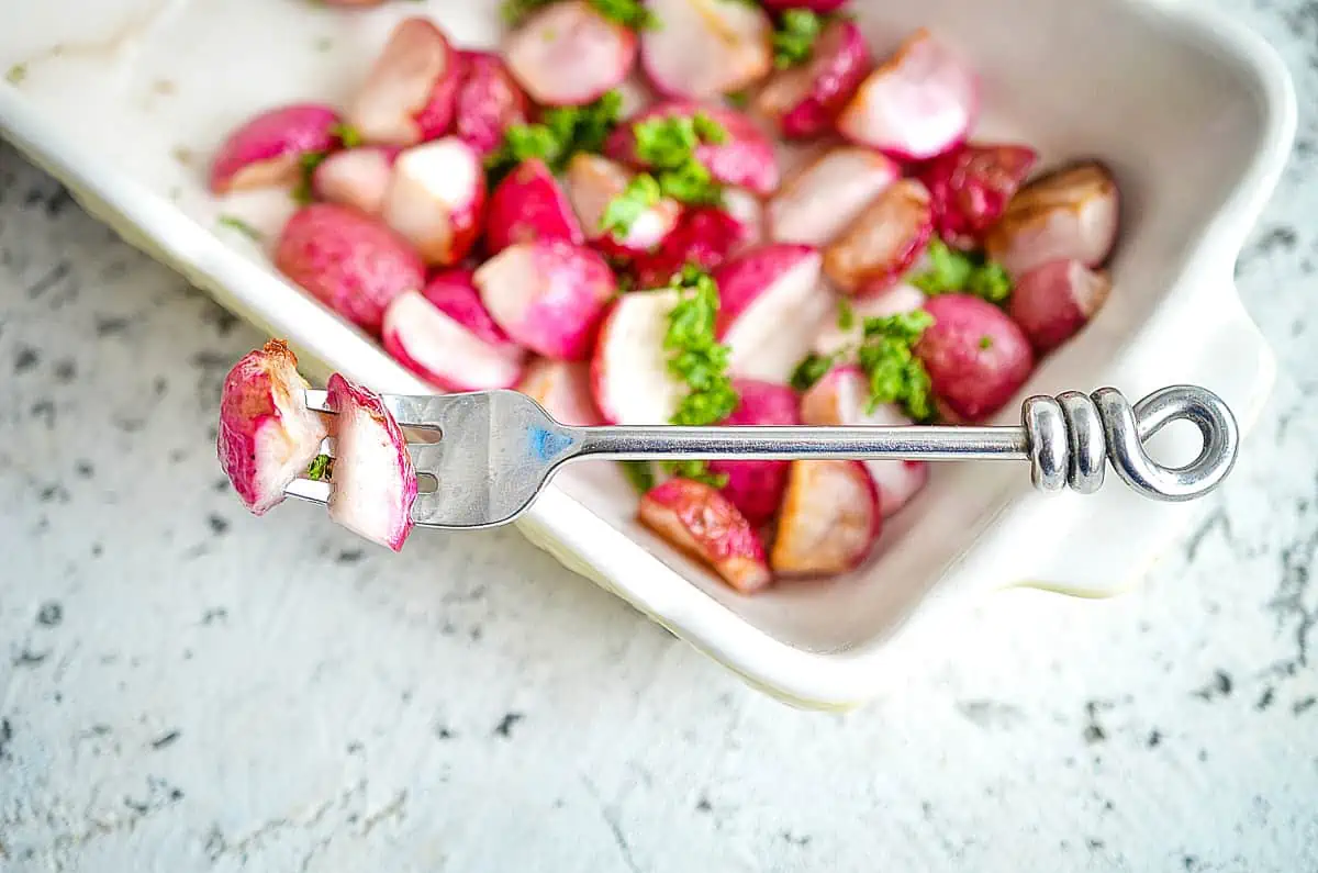 Roasted radishes in a white dish with a fork.