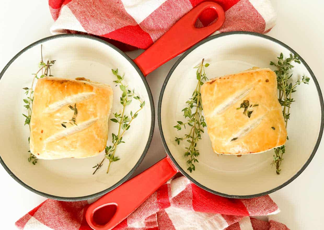 Two sausage rolls with thyme on a red and white checkered tablecloth, perfect for winter dinners.