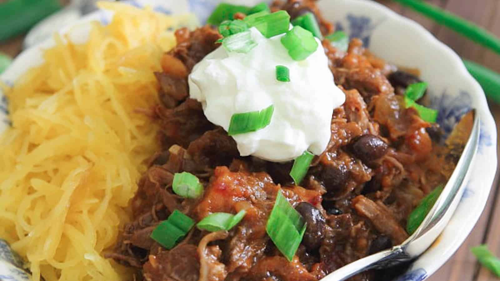 A bowl of chili with noodles and sour cream.