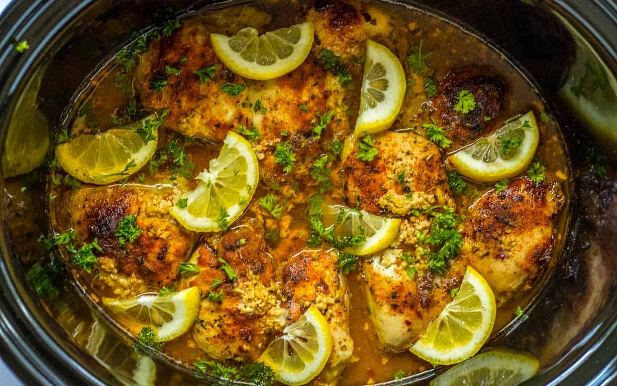 A crock pot filled with chicken and lemons.