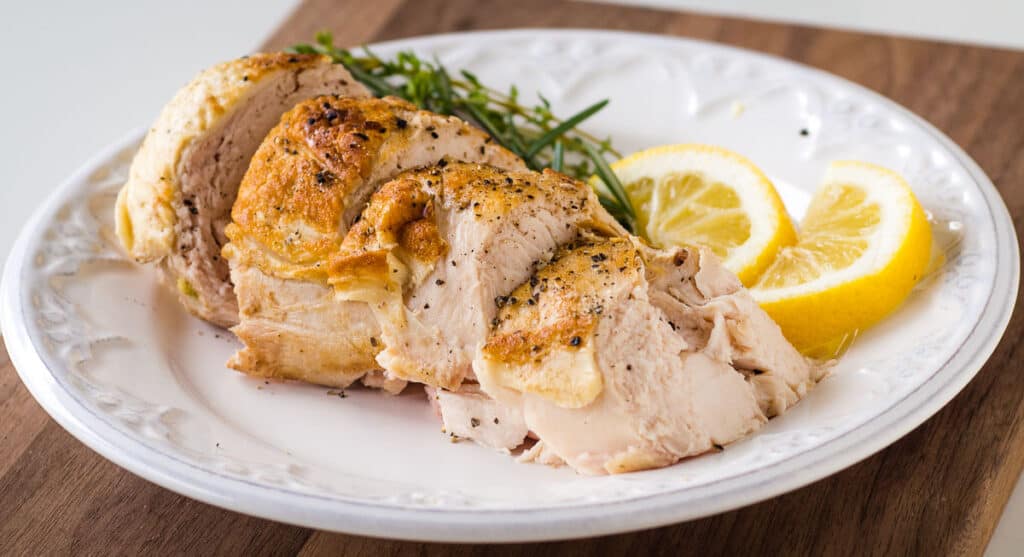 Sous vide cooked sliced chicken on a white plate with lemon slices.