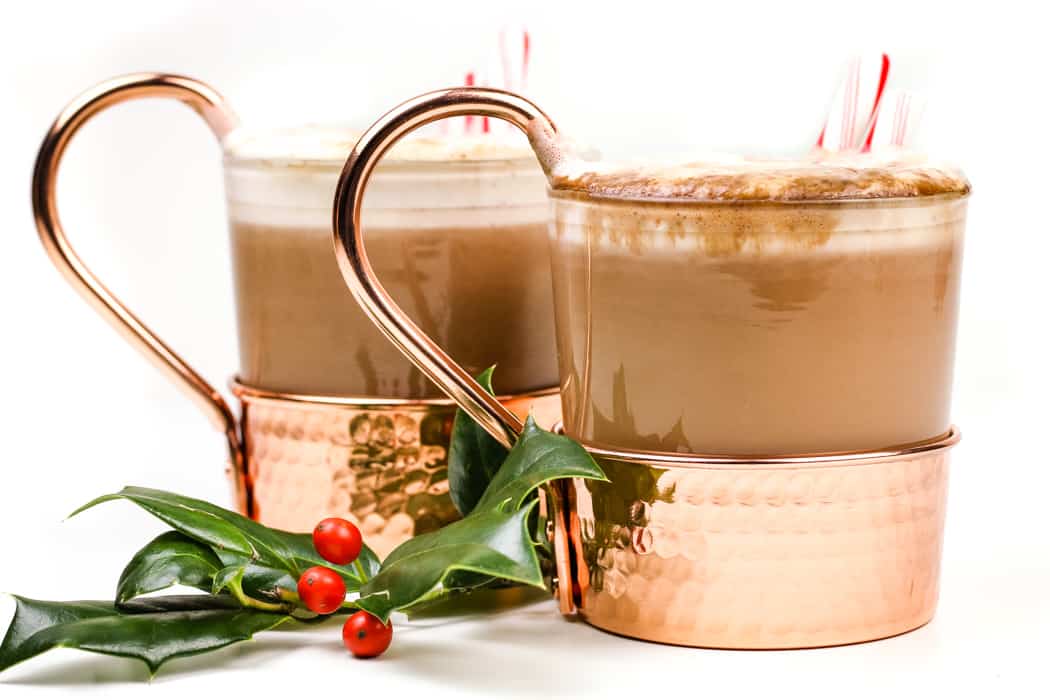 Two copper mugs of hot chocolate with whipped cream and candy canes.