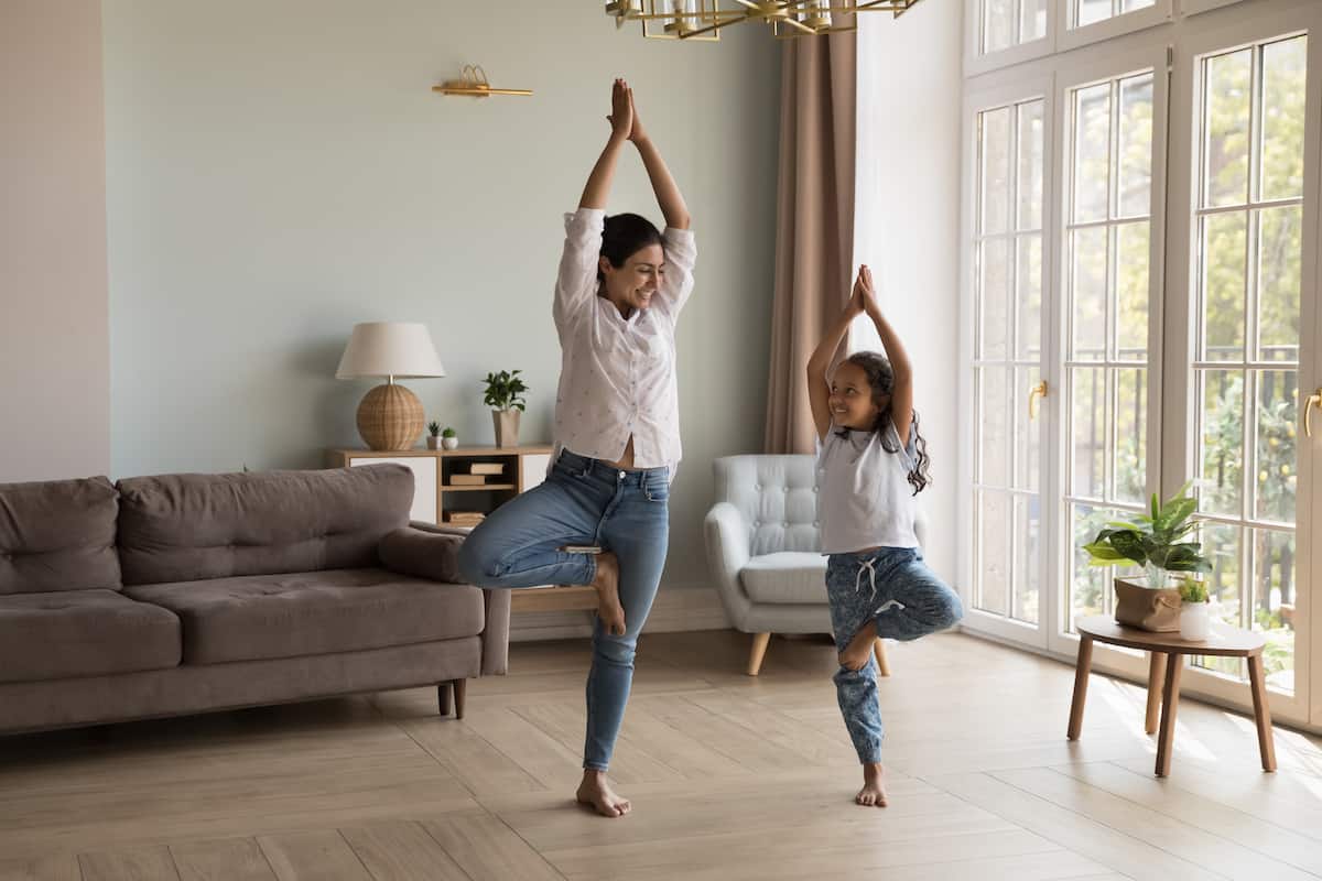 A mother and daughter doing yoga in a living room.