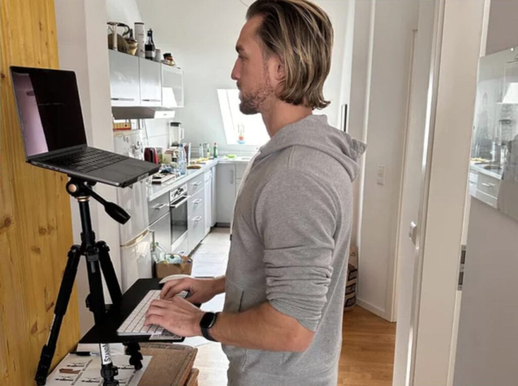 A man using a laptop on a standing desk in a kitchen.