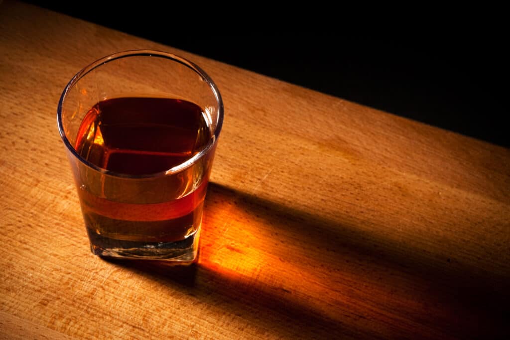 A glass of whiskey on a wooden table.