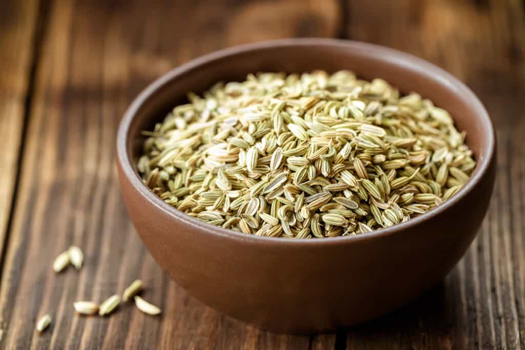 Fennel seeds in a brown bowl on a wooden table.