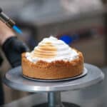 A person is toasting meringue on a cake with a torch.