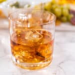 A glass of whiskey with ice and grapes on a marble table.