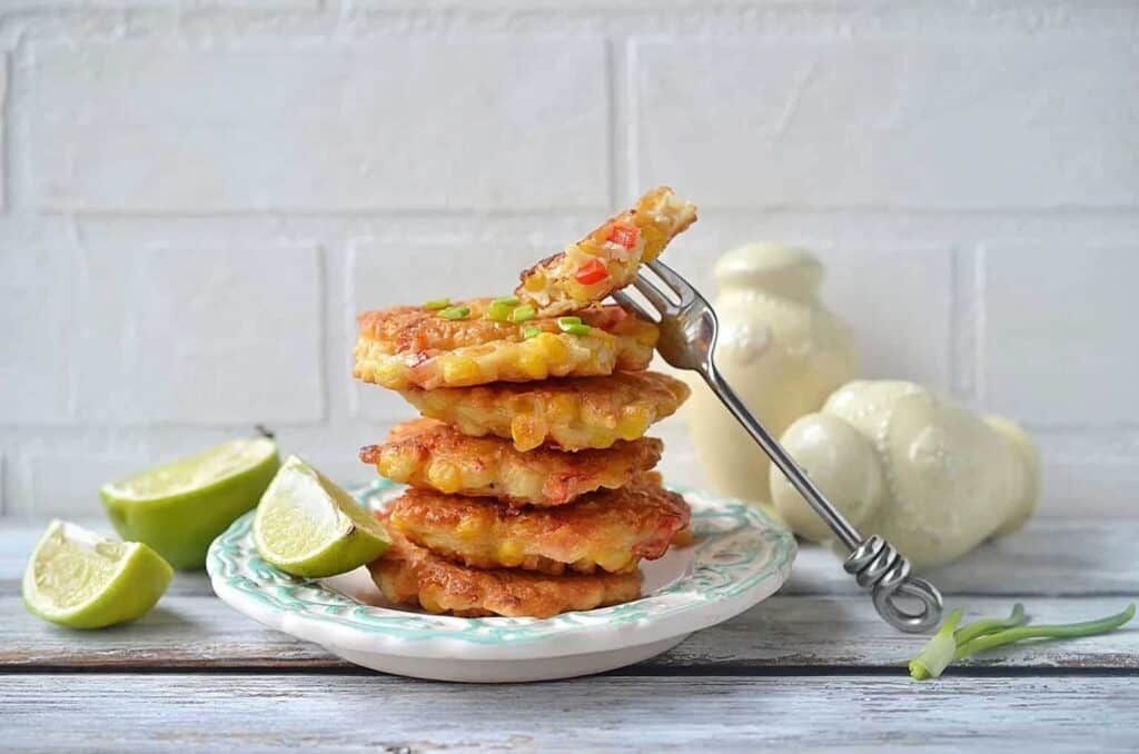 A stack of corn fritters on a plate with lime wedges.