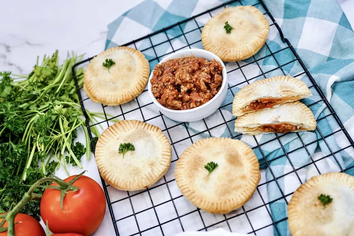 A tray of Sloppy Joe Hand Pies on a cooling rack with tomatoes and herbs.