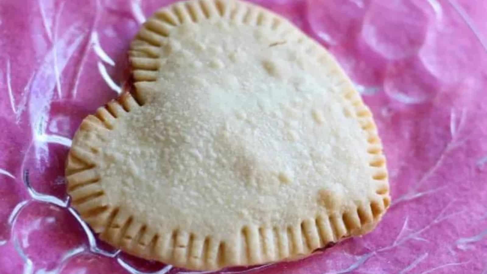 Heart shaped pop tart on a glass plate with a pink background.