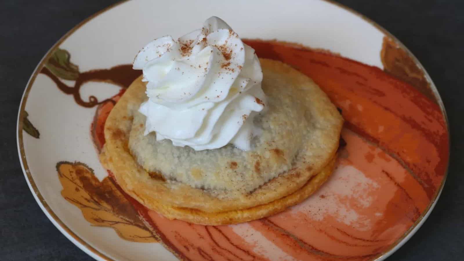 Pumpkin pie pop tart with whipped cream on top on a pumpkin plate.