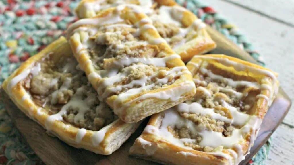 A plate of apple crumb pastries with icing on top.