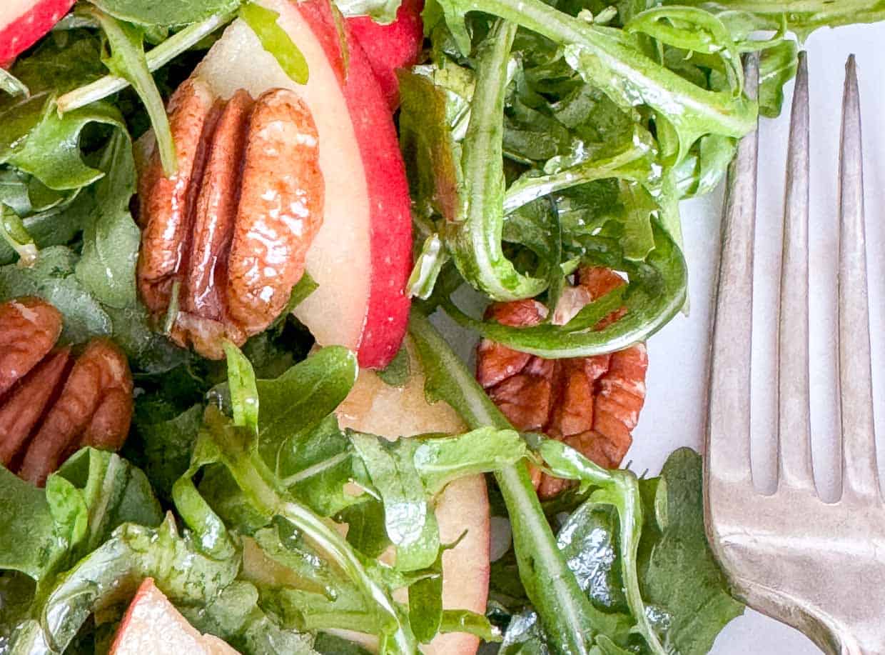 A salad on a plate with apples, pecans, and a fork.