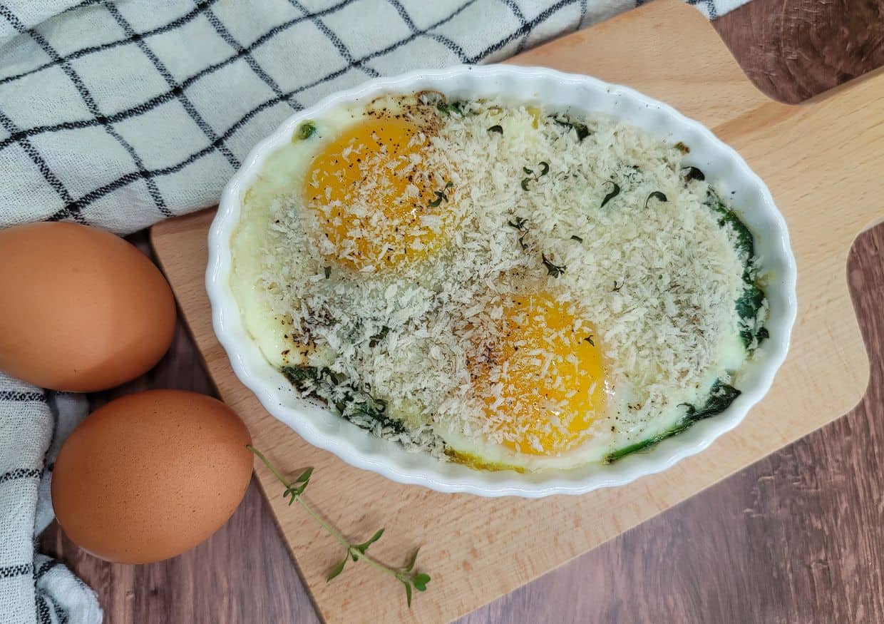 Baked eggs with spinach and parmesan on a wooden cutting board.