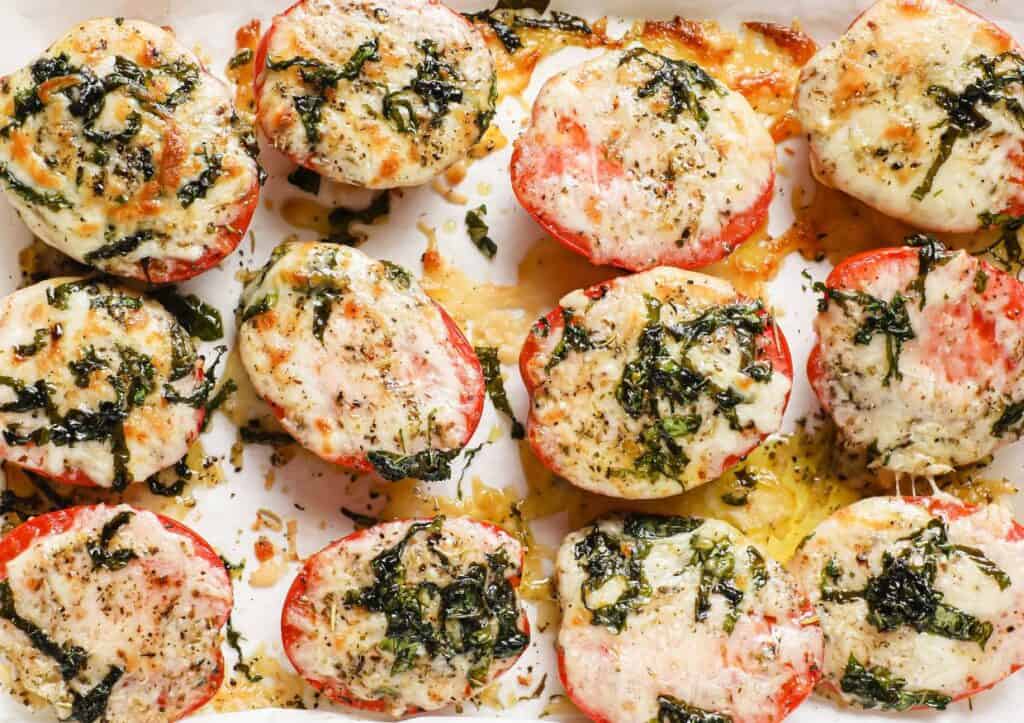 Tomatoes stuffed with cheese and basil on a baking sheet.