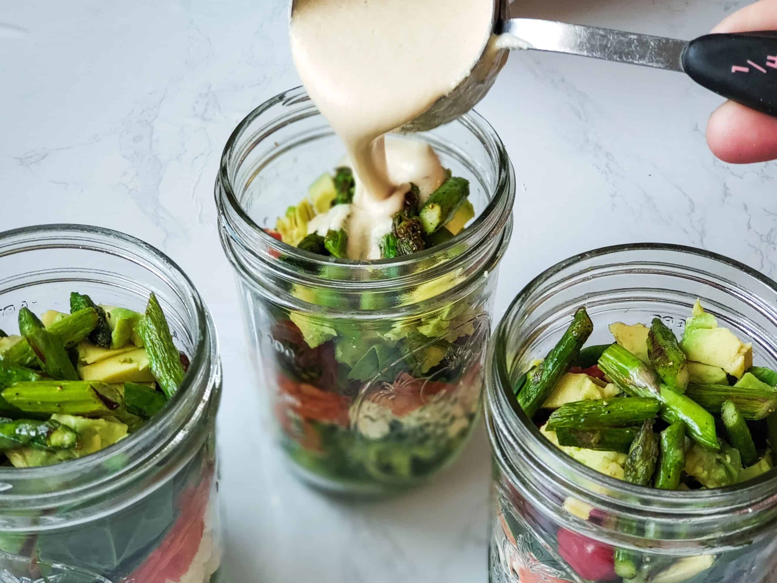 Three jars of salad, pouring dressing on top.