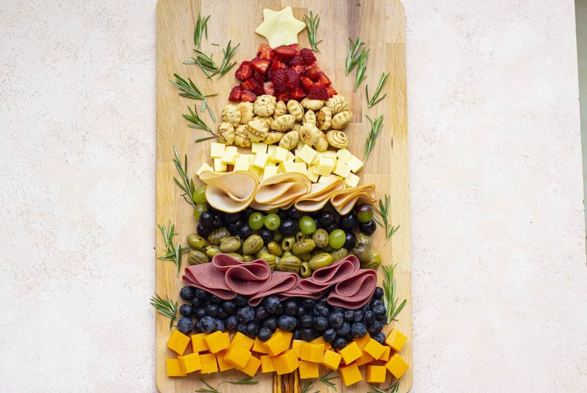 A Christmas tree made of cheese, fruit, and peach cupcakes on a wooden board.