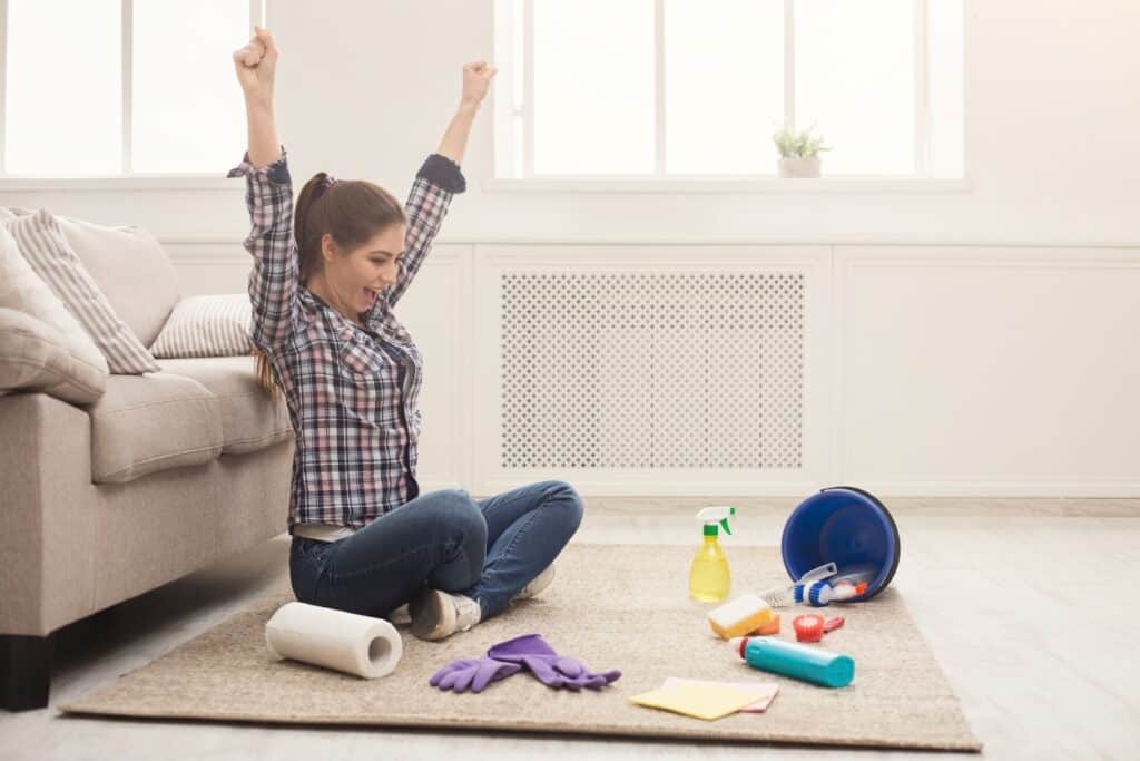 A woman is sitting on the floor with cleaning supplies.