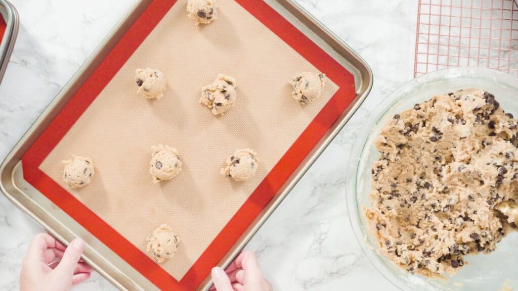 A person is putting cookies on a silicone baking sheet.