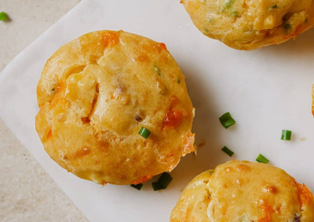 Three muffins on a white plate with green onions.