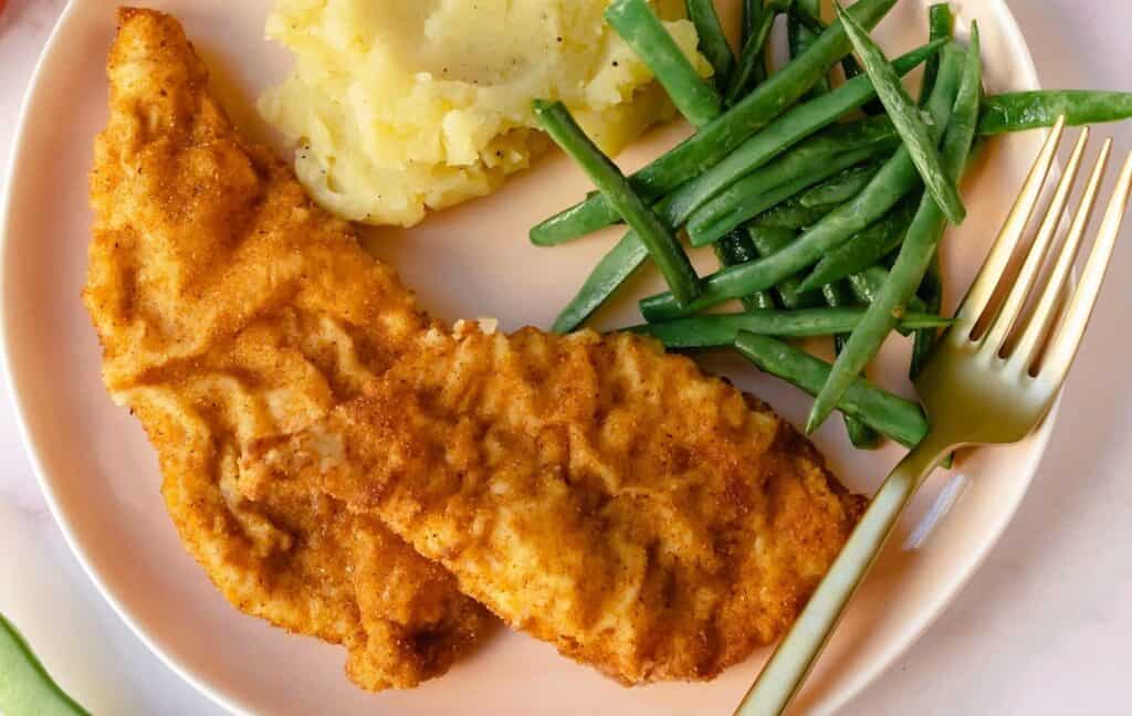 Fried chicken with mashed potatoes and green beans on a plate with a fork.