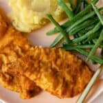 Fried chicken with mashed potatoes and green beans on a plate with a fork.