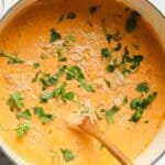 A pot of soup with parmesan cheese and parsley.