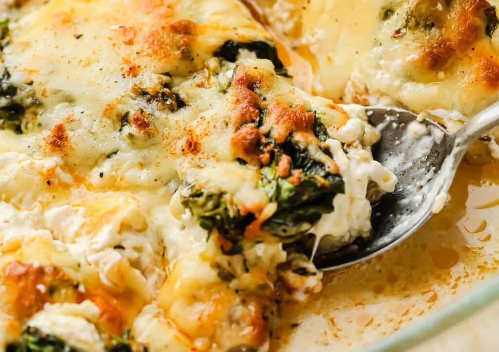 A dish of cheesy spinach casserole with a spoon.