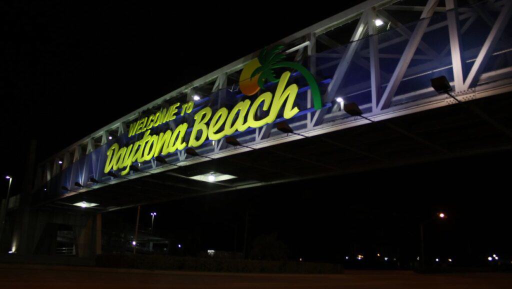 A sign that says welcome to Daytona Beach is lit up at night.