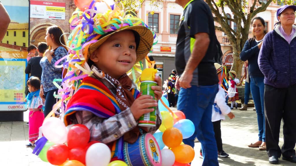A child in a vibrant costume holding a balloon at a colorful celebration in Mexico City.