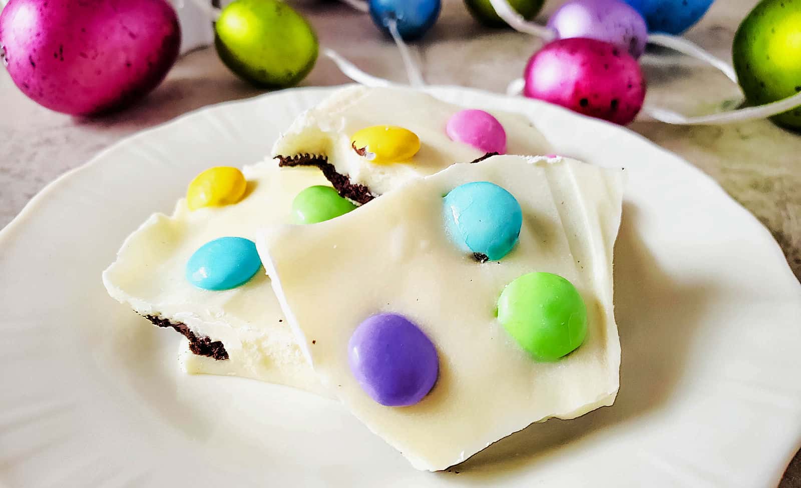 Easter chocolate bark on a white plate with colorful easter eggs.