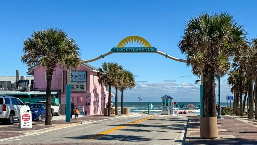 A vibrant street lined with palm trees and a prominent sign leading to the beach, offering enticing things to do in New Smyrna Beach.