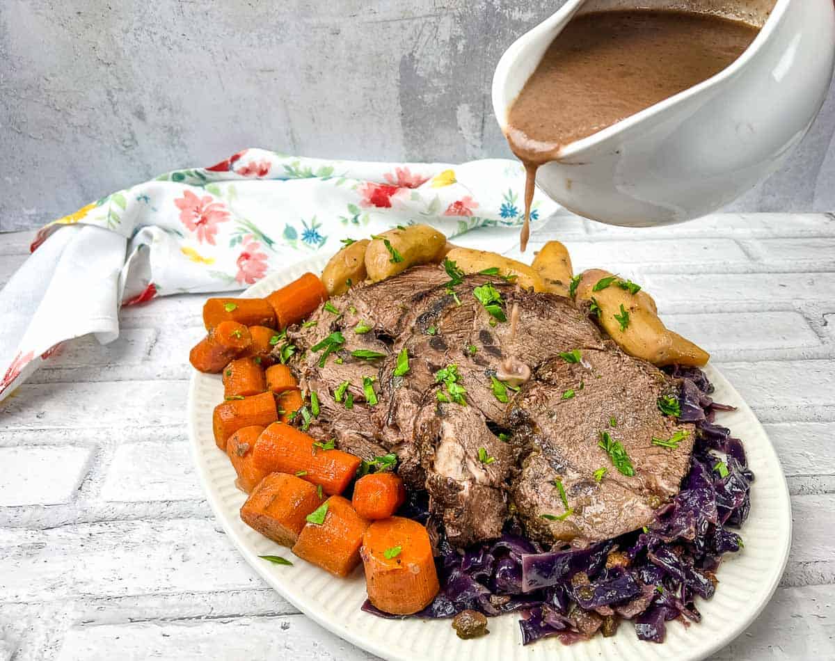 A plate of German pot roast beef with a sauce being poured over it.