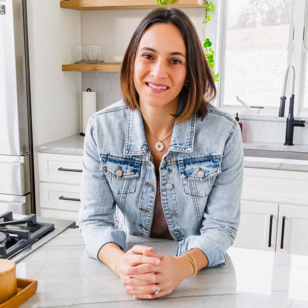 A woman in a denim jacket sitting in a kitchen.