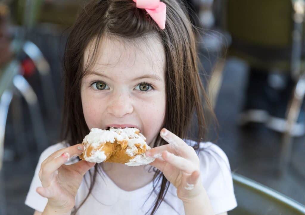 A little girl indulging in a delectable donut during a Mardi Gras celebration at a restaurant.