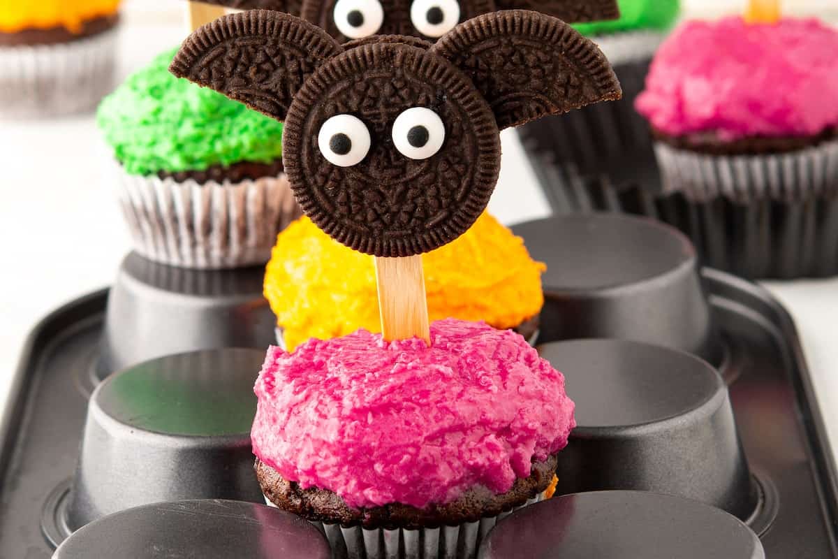 Several colorful cupcakes with oreos shaped as bat.