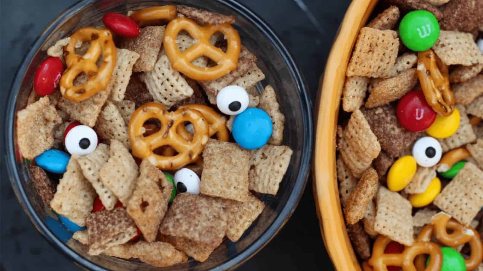 Glass bowl of monster chex mix next to a yellow bowl.