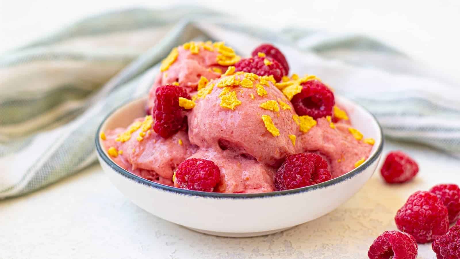 A bowl of frozen yogurt with raspberries and corn flakes.